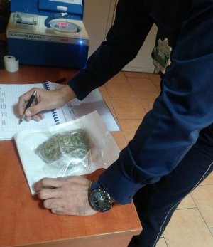 Policjant ewidencjonuje zatrzymane narkotyki. W plastikowej paczce widać zabezpieczony susz roślinny.