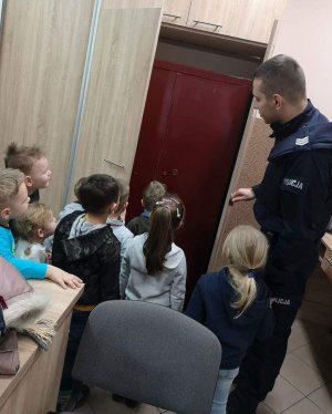 Policjant pokazuje przedszkolakom metalową szafę, w której przechowywane są akta prowadzonych spraw.