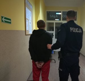 Korytarz w Komendzie Powiatowej Policji w Żninie. Z prawej strony policjant, z lewej strony zatrzymany sprawca rozboju.