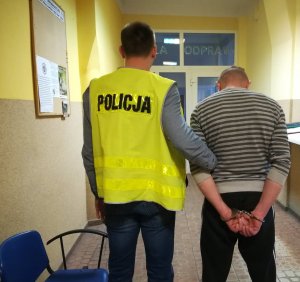 Z lewej strony policjant ubrany w żółtą kamizelkę, z prawej zatrzymany do sprawy kradzieży elektronarzędzi.