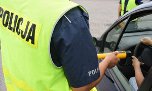 Policjant ubrany w żółtą kamizelkę przy użyciu alkomatu sprawdza trzeźwość kierowcy.