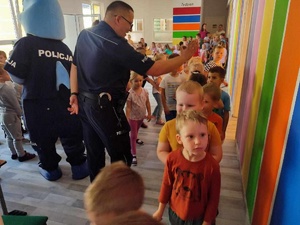 Policjant przybija piątki z przedszkolakami. Za jego plecami policyjny Polfinek, podczas interakcji z dziećmi.