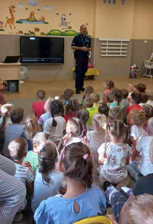 Policjant podczas prelekcji. Przed nim zgromadzone na dywanie dzieci.