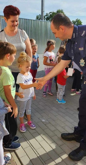 Policjant wita się z dziećmi przed budynkiem przedszkola w Rogowie.