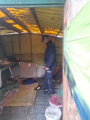 Policjant znajduje się w środku komórki, w której na co dzień przebywają bezdomni. Widoczne na zdjęciu są koce i poduszki, a na podłodze butelka po alkoholu.