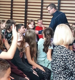 Dzielnicowy podczas wystąpienia przekazuje mikrofon uczniom, którzy zadają pytania.