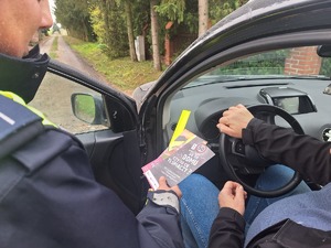 policjant wręcza materiały informacyjne i odblaski kierowcy