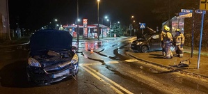 Na pierwszym planie uszkodzony samochód marki Opel. Z prawej strony na chodniku pojazd marki Daihatsu i strażacy.