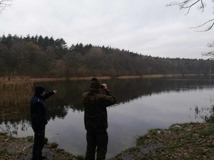 Funkcjonariusz Policji i Państwowej Straży Rybackiej z Bydgoszczy stoją na brzegu jeziora. Obserwują co dzieje się na wodzie.